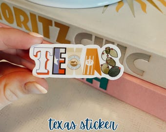 May include: A sticker featuring the word "TEXAS" spelled out in colourful letters. Each letter is decorated with a different image representing Texas, including a bluebonnet, a cowboy boot, a cactus, and a star. The sticker is on a pink and white surface.