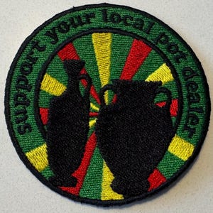 May include: A round green, yellow, and red embroidered patch with the text "Support your local pot dealer" in a circle around two black silhouettes of pottery.
