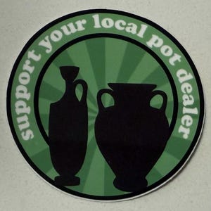 May include: A round sticker with the text "support your local pot dealer" in white lettering. The sticker features two black silhouette pottery vessels against a green radial background.