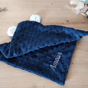 Op de afbeelding: Een donkerblauwe babydeken met witte pompoenen en het woord "Amour" geborduurd in wit.