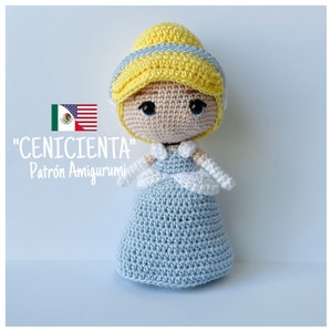 Puede incluir: Una muñeca de ganchillo de Cenicienta con un vestido azul claro con detalles blancos y una corona amarilla. La muñeca está de pie sobre un fondo azul claro. El texto "CENICIENTA" y "Patrón Amigurumi" está escrito debajo de la muñeca.