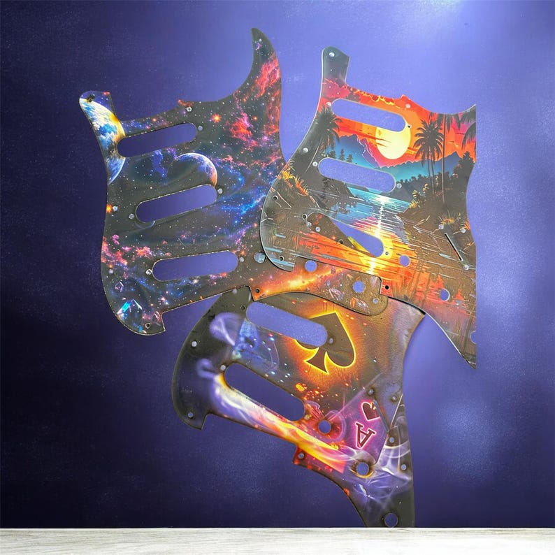 May include: Three guitar pickguards with unique designs. One features a galaxy scene with planets, another a tropical sunset with palm trees, and the third a playing card theme with an Ace of Spades.