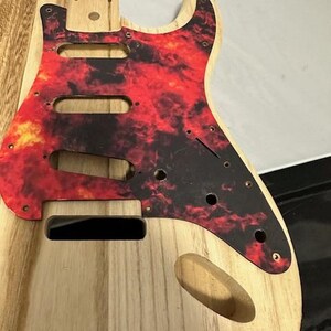 May include: Unfinished wooden guitar body with a red and black flame pattern pickguard.