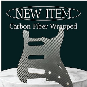 May include: A black carbon fiber guitar body with a textured finish. The body has a cut-out for a pickup and a control knob. The text "NEW ITEM" and "Carbon Fiber Wrapped" is visible above the guitar body.