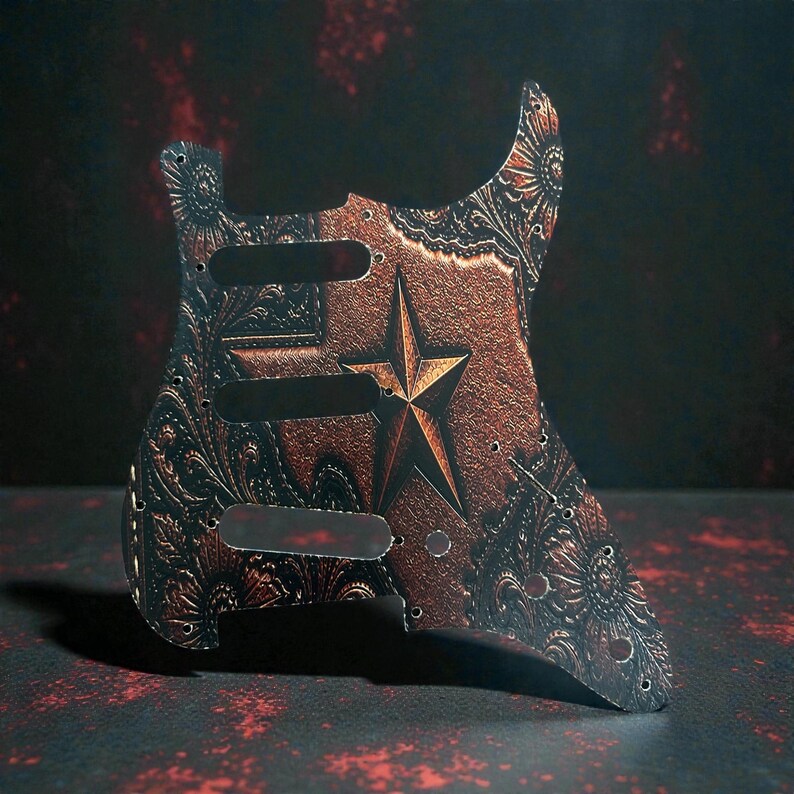 May include: A guitar pickguard with a copper-colored finish and a star design. The pickguard has a floral pattern and three pickup cutouts. The star is in the center of the pickguard.