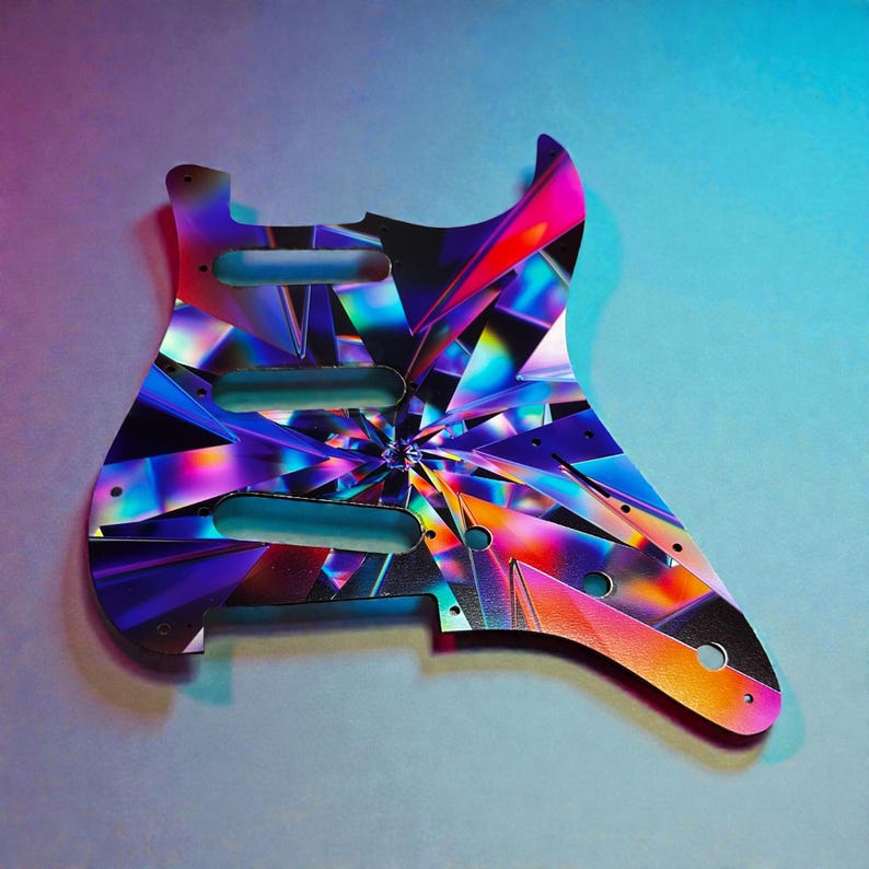 May include: A colorful guitar pickguard with a vibrant, geometric design. The pickguard features a spectrum of colors, including pink, purple, blue, and orange, arranged in a fractured, crystalline pattern. It has three pickup holes and mounting screw holes.
