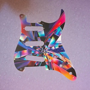 May include: A colorful guitar pickguard with a geometric, prism-like design. The pickguard features a vibrant array of colors including pink, blue, orange, and purple. It has three pickup cutouts and several screw holes for mounting.