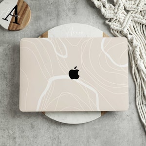 Op de afbeelding: Een laptop met een abstract ontwerp in wit en roze op de deksel. De laptop staat op een witte marmeren onderzetter.