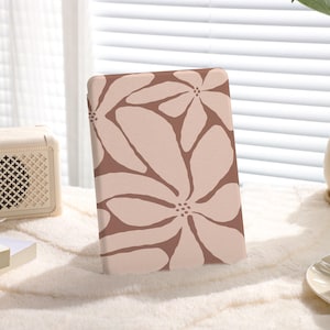 May include: A pink and brown floral patterned case for an e-reader. The case is sitting on a white fuzzy surface.