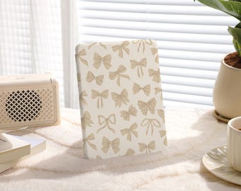 Op de afbeelding: Een witte notebookhoes met een patroon van beige strikken en vlinders. De hoes is gemaakt van glad, mat materiaal.