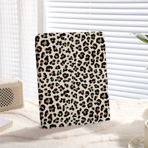 Puede incluir: Una funda para tablet blanca con un diseño de estampado de leopardo marrón y negro.