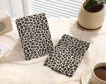 May include: Two leopard print tablet cases, one larger than the other, are lying on a white fuzzy surface. The cases are made of a soft, flexible material and have a brown and black leopard print design.
