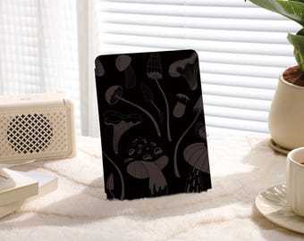 May include: Black and white illustration of mushrooms on a dark background. The illustration is printed on a black case for an e-reader.