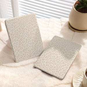 May include: Two beige tablet cases with a leopard print design. The cases are lying on a white fuzzy surface.