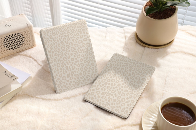 May include: Two beige tablet cases with a leopard print design. The cases are lying on a white fuzzy surface.