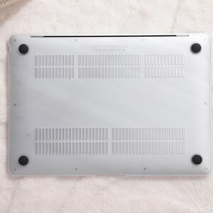 May include: The bottom of a white laptop computer with a silver trim and black rubber feet. The laptop has a series of small holes for ventilation.