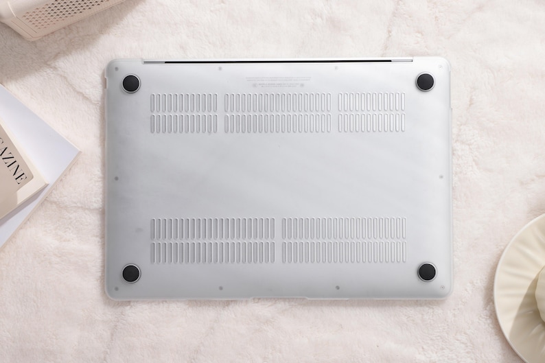 May include: The bottom of a white laptop computer with a silver trim and black rubber feet. The laptop has a series of small holes for ventilation.