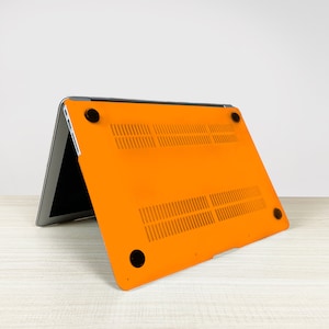 May include: Orange laptop case with a textured design and black rubber feet. The case is open and the laptop is visible inside.