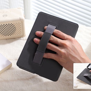 May include: A black tablet case with a gray elastic hand strap. The strap is designed to be held with one hand.