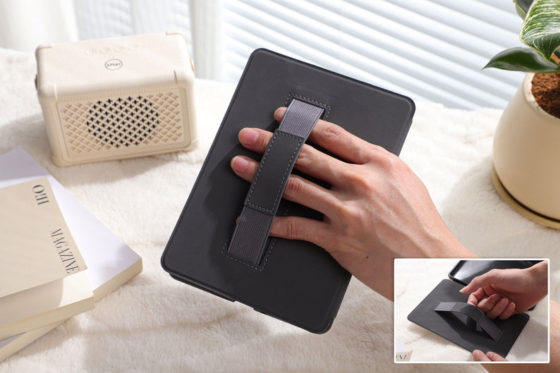 May include: A black tablet case with a gray elastic hand strap. The strap is designed to be held with one hand.