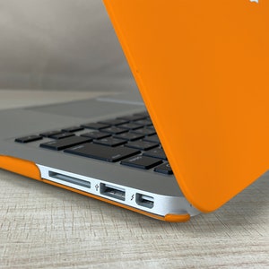May include: A close-up of a silver laptop with a bright orange case. The laptop is open and the keyboard is visible. The laptop has a USB port, a charging port, and a headphone jack.