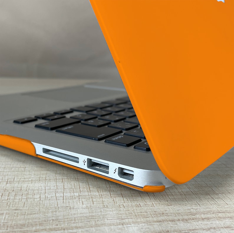 May include: A close-up of a silver laptop with a bright orange case. The laptop is open and the keyboard is visible. The laptop has a USB port, a charging port, and a headphone jack.