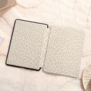 May include: An e-reader with a beige leopard print cover. The e-reader is open and the screen is visible. The e-reader is on a white fuzzy surface.