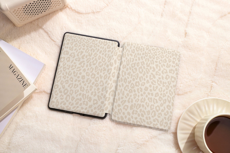 May include: An e-reader with a beige leopard print cover. The e-reader is open and the screen is visible. The e-reader is on a white fuzzy surface.