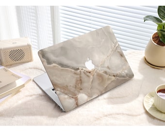 Peut inclure: Un ordinateur portable avec une peau à motif marbré. La peau est gris clair avec des veines brunes. L'ordinateur portable est fermé et posé sur une surface blanche.