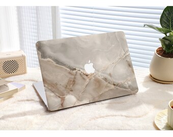 Peut inclure: Un ordinateur portable avec une peau à motif marbré. La peau est de couleur gris clair avec des veines brunes. L'ordinateur portable est fermé et posé sur une surface blanche.