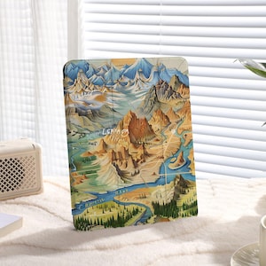 May include: A vintage-style illustration of a mountain range with a river winding through it. The illustration is printed on a tablet case, which is standing upright on a white surface.
