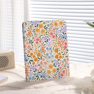 Puede incluir: Una funda para tablet blanca con un patrón floral con flores rosas, amarillas, azules y naranjas sobre un fondo blanco.