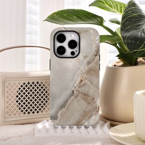 May include: A white and brown marble phone case with a black camera lens cutout. The case is designed for an iPhone.