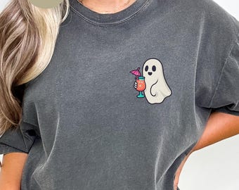 May include: A charcoal gray crewneck t-shirt featuring a small graphic on the left chest of a white ghost holding a tropical cocktail with a pink umbrella. The shirt has a faded, vintage-style wash and the text PEPPER is printed in a circle.