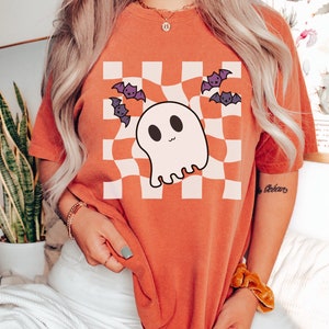 May include: Orange t-shirt with a white and black checkered pattern featuring a cartoon ghost and bats. The text "Boo" is written on the sleeve.