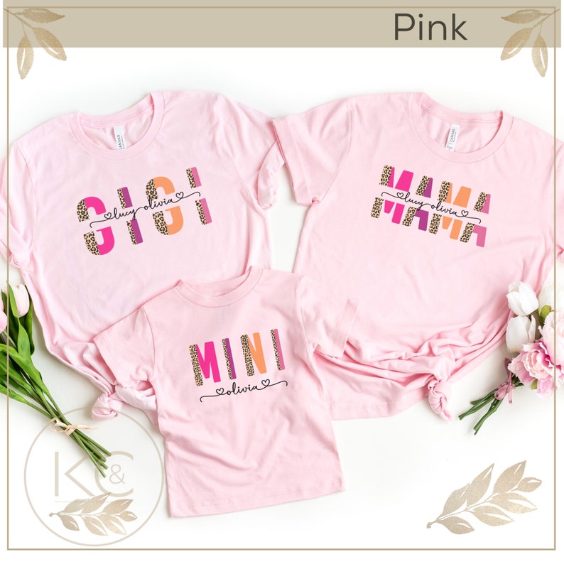 May include: Three pink t-shirts with the words "SISI", "MAMA", and "MINI" in colorful block letters with leopard print accents. The shirts are personalized with the name "Lucy Olivia" in a smaller font.