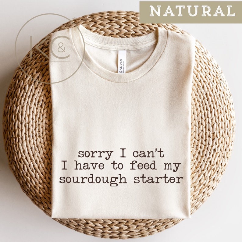 May include: A natural colored t-shirt with the text "sorry I can't I have to feed my sourdough starter" printed on the front.