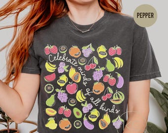 May include: A charcoal gray t-shirt featuring a colorful graphic print of various fruits and vegetables, including strawberries, bananas, grapes, and eggplants. The text "Celebrate minds of all kinds" is written in white cursive script across the center.