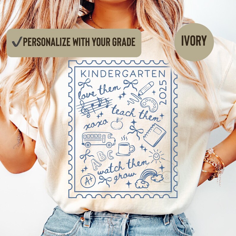 May include: Ivory t-shirt with a blue stamp design, featuring the word "KINDERGARTEN" and school-themed illustrations. The text "love them, teach them, watch them grow" is included. The shirt also has the text "PERSONALIZE WITH YOUR GRADE" and "2025".