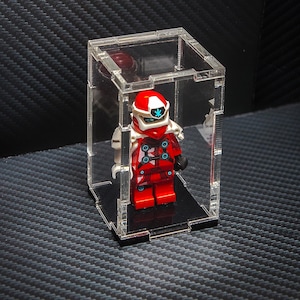 May include: A red and white Lego minifigure with a snowflake design on its helmet is displayed in a clear acrylic display case.