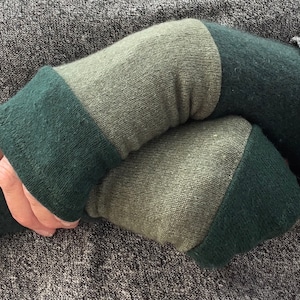 Può includere: Un paio di scaldamani a righe verdi e verde oliva. Gli scaldamani sono realizzati in un tessuto morbido e lavorato a maglia.