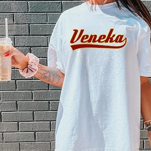May include: White t-shirt with the name "Veneka" in a red vintage-style font. The shirt is oversized and has a relaxed fit.