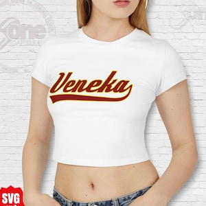 May include: White crop top with short sleeves featuring the word "Veneka" in a red and gold baseball-style font.