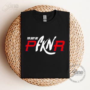 May include: Black t-shirt with white text that says "Yo soy de" and "PFKN" in red and blue letters.