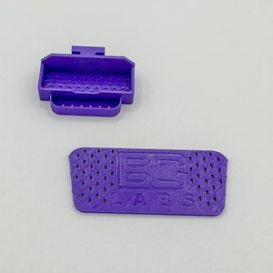 Puede incluir: Dos piezas de plástico morado impresas en 3D con un patrón de rejilla. La pieza más grande tiene el texto "EC LABS" impreso en ella.