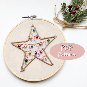 Puede incluir: Un aro de bordado blanco con un diseño de árbol de Navidad en forma de estrella. El árbol está hecho de ramitas y decorado con cuentas de colores y hilo de bordar. El texto "PDF Pattern" está escrito en rosa sobre un fondo blanco.