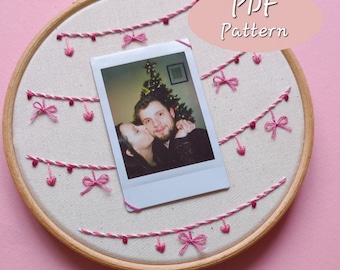 May include: A white embroidery hoop with a pink and white embroidered garland design. A Polaroid photo of a couple is centered in the hoop. The text "PDF Pattern" is written in pink on a white oval in the upper right corner of the hoop.