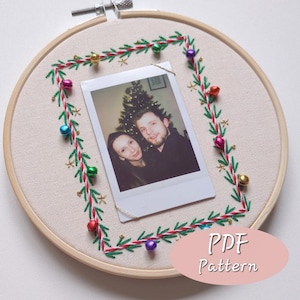 Puede incluir: Un bastidor bordado con una fotografía de una pareja. La foto está enmarcada por un bordado verde y rojo con pequeñas estrellas doradas y campanas de colores. El texto "PDF Pattern" es visible.