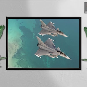 May include: A framed print showing two grey fighter jets flying over turquoise water. The jets are in mid-flight, with their wings and tails visible. The print is from the Minibot Print Shop.