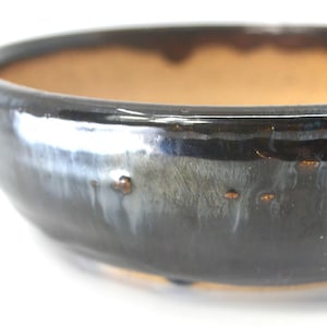 May include: A glazed ceramic bowl with a dark blue exterior and a light brown interior. The bowl has a wide, shallow shape and a glossy finish. The exterior has a textured appearance with small, raised spots.
